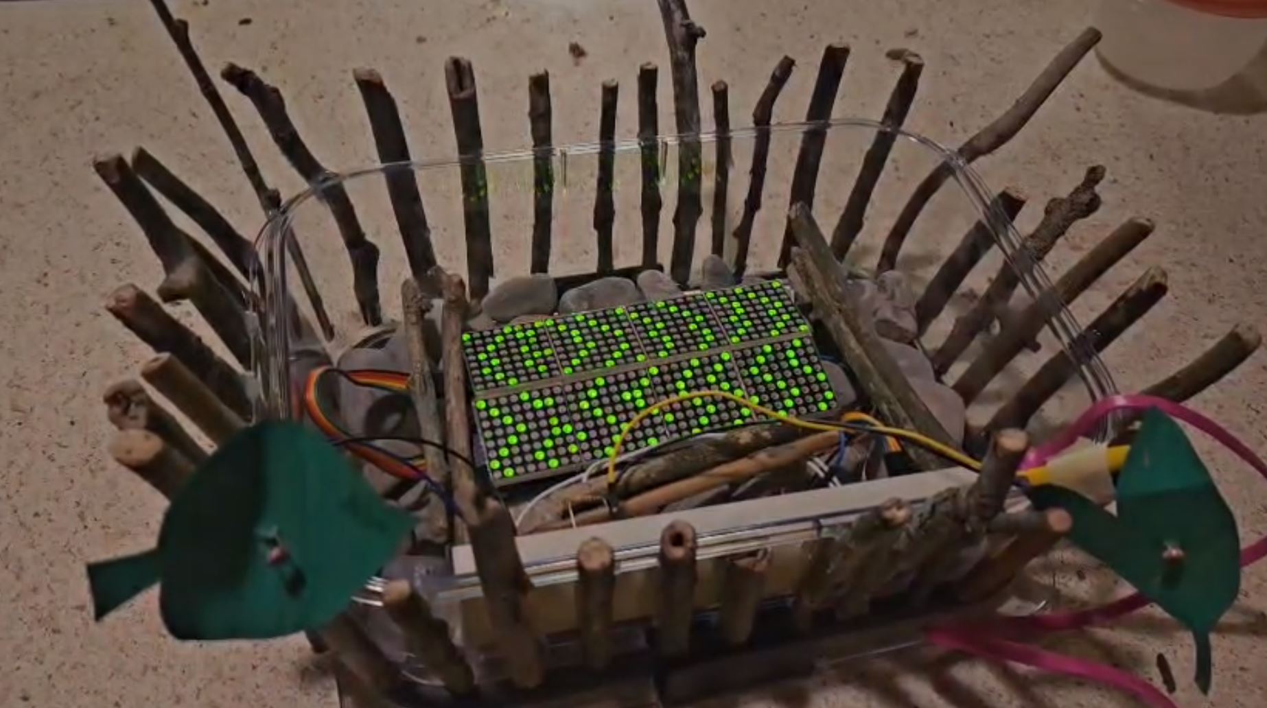 Picture of a wave simulation running on an arduino, in a dish covered in sticks and rocks to look like a pond or creek. 