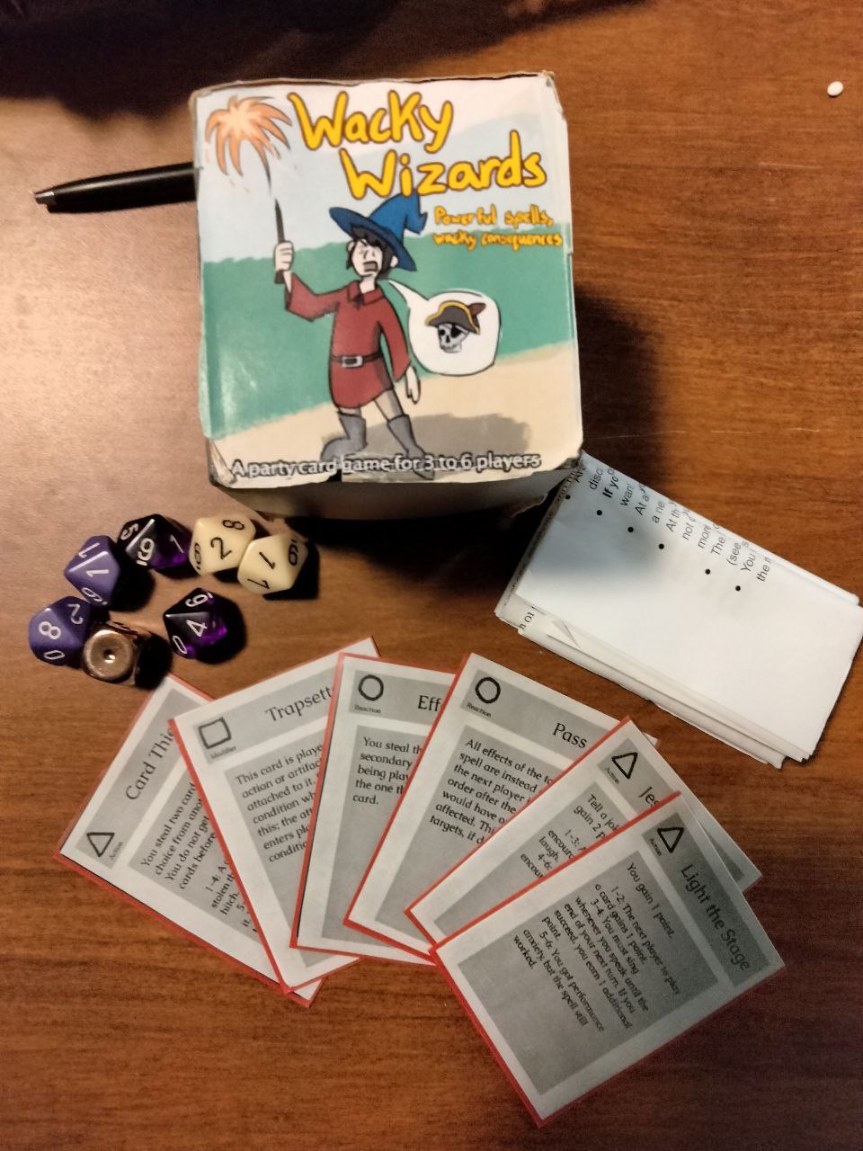 Image of the cards, dice, rules sheet, and box for Wacky Wizards displayed on a wood table